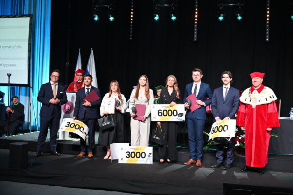 Laureaci konkursu Laury Akademickie stojący w rzędzie z Rektorem trzymają symbole otrzymanych nagród i dyplomy, zdjęcie zrobione w trakcie uroczystej inauguracji